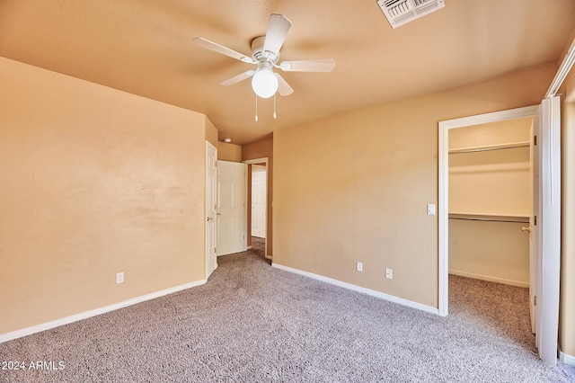 unfurnished bedroom with a walk in closet, ceiling fan, a closet, and carpet