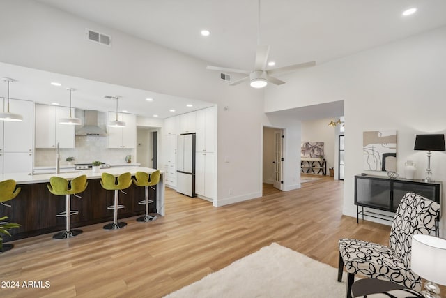 kitchen featuring a kitchen breakfast bar, wall chimney exhaust hood, hanging light fixtures, white cabinets, and white fridge