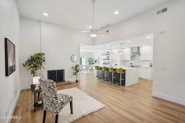 living room with a high ceiling, ceiling fan, and light hardwood / wood-style flooring