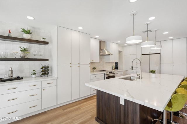 kitchen with stainless steel electric range, wall chimney exhaust hood, sink, and a kitchen island with sink