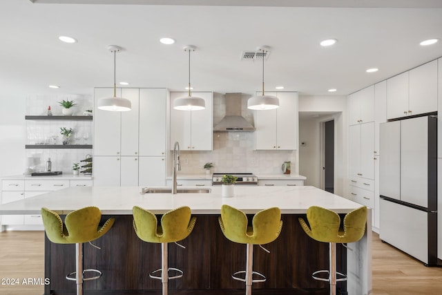 kitchen with hanging light fixtures, wall chimney exhaust hood, white fridge, and a large island with sink