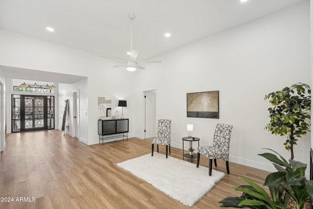 living area featuring light hardwood / wood-style floors, ceiling fan, and a high ceiling