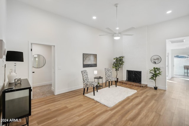 living area featuring a fireplace, ceiling fan, and light hardwood / wood-style flooring