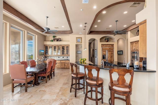kitchen with visible vents, arched walkways, dark countertops, a ceiling fan, and a breakfast bar