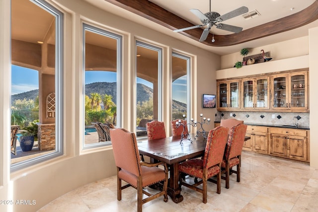 dining space with a raised ceiling, a mountain view, a ceiling fan, and visible vents