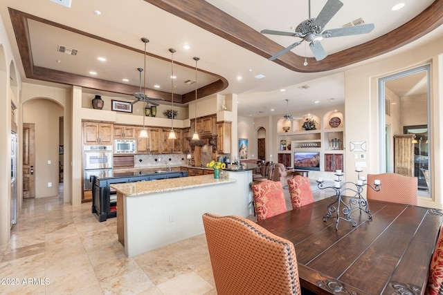 kitchen featuring visible vents, built in features, a raised ceiling, arched walkways, and appliances with stainless steel finishes