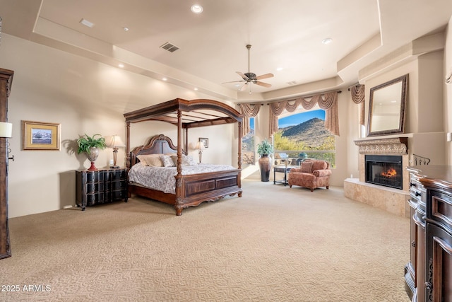 bedroom with visible vents, a raised ceiling, carpet, and a lit fireplace