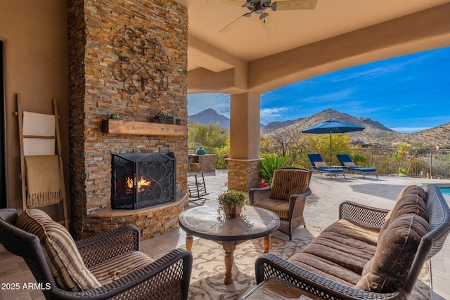 view of patio with a mountain view, ceiling fan, fence, and an outdoor stone fireplace