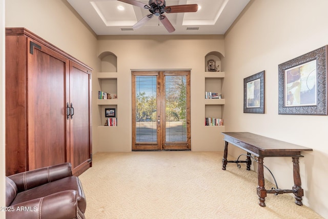 office space with visible vents, built in shelves, a ceiling fan, coffered ceiling, and light carpet