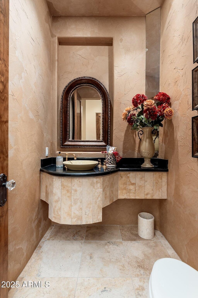 bathroom with toilet, vanity, a textured wall, and stone finish flooring