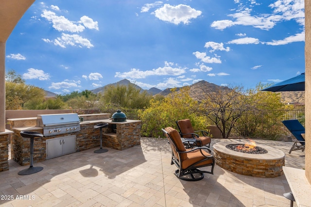 view of patio with area for grilling, an outdoor fire pit, fence, exterior kitchen, and a mountain view