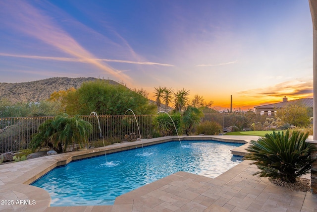 pool at dusk featuring a patio area, a mountain view, fence, and a fenced in pool