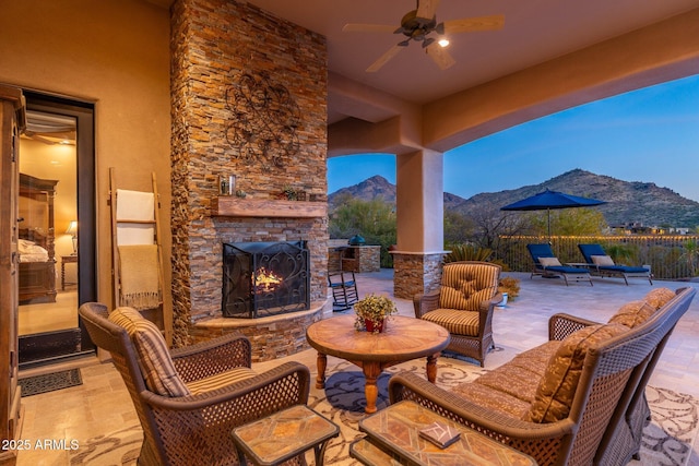 view of patio featuring fence, an outdoor stone fireplace, a mountain view, and a ceiling fan