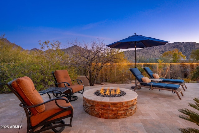 patio terrace at dusk featuring fence, a fire pit, and a mountain view