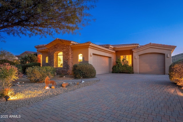 mediterranean / spanish home featuring a tiled roof, stucco siding, decorative driveway, stone siding, and a garage