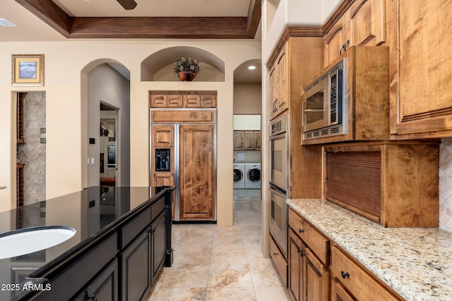 kitchen with built in appliances, light stone countertops, visible vents, brown cabinetry, and washing machine and clothes dryer