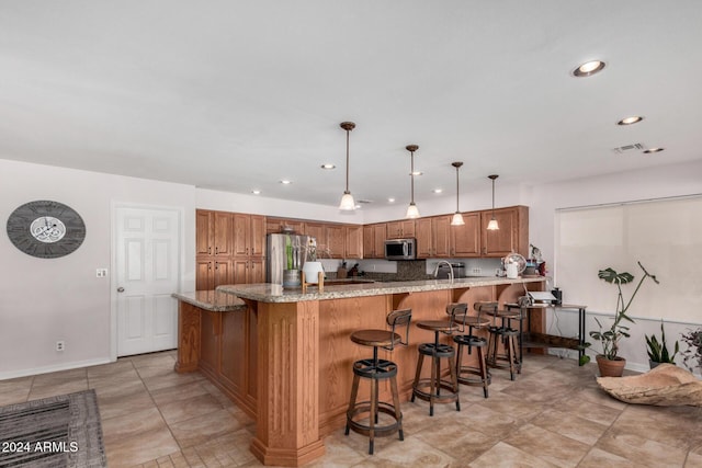 kitchen with a kitchen breakfast bar, light stone counters, pendant lighting, and appliances with stainless steel finishes