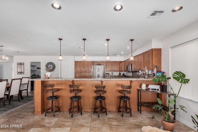 kitchen with sink, light stone counters, kitchen peninsula, decorative light fixtures, and appliances with stainless steel finishes