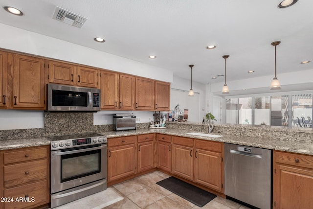 kitchen featuring pendant lighting, sink, light stone countertops, and stainless steel appliances