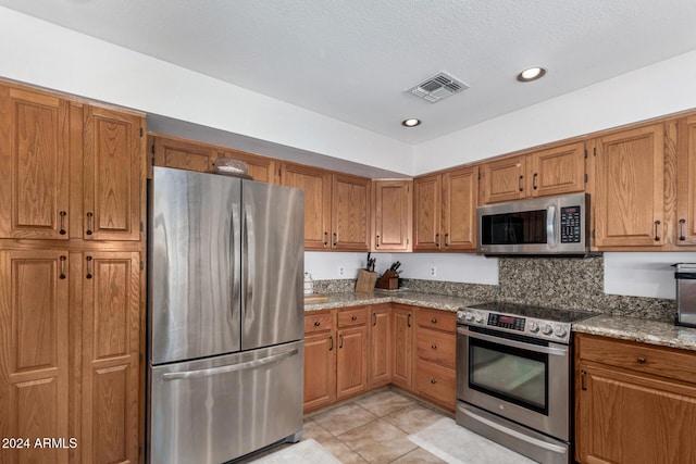 kitchen featuring light tile patterned flooring, light stone countertops, backsplash, and appliances with stainless steel finishes