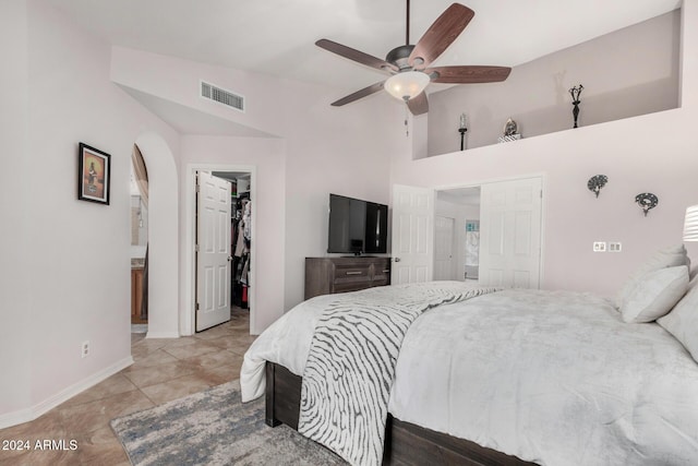 bedroom with a walk in closet, vaulted ceiling, ceiling fan, light tile patterned floors, and a closet