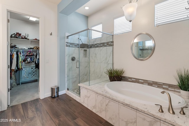 bathroom with a garden tub, a spacious closet, a stall shower, wood finished floors, and baseboards