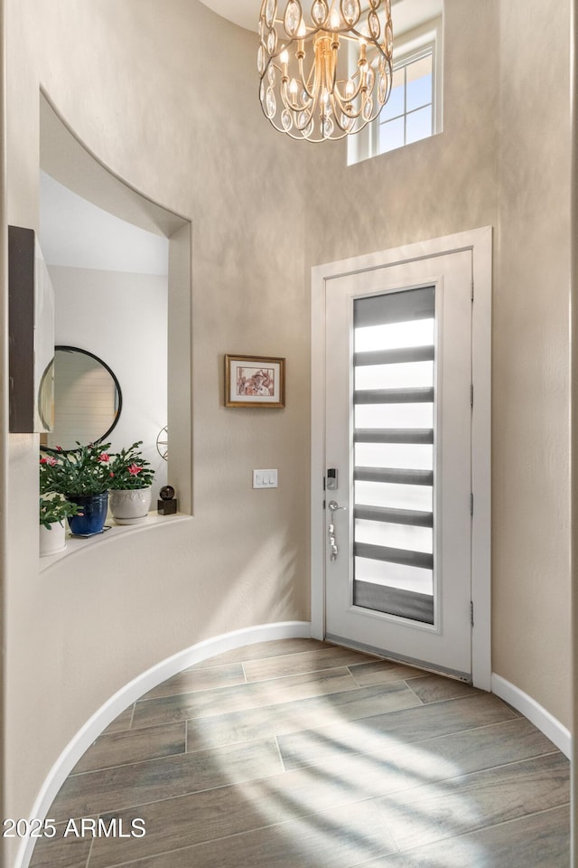 foyer with a notable chandelier, a high ceiling, wood finished floors, and baseboards