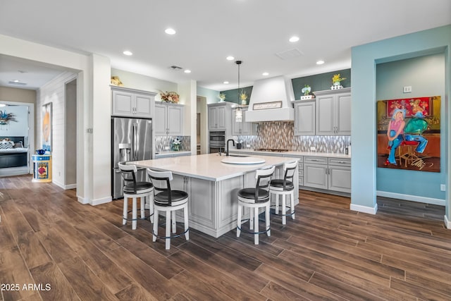 kitchen with a kitchen breakfast bar, light countertops, appliances with stainless steel finishes, gray cabinets, and custom range hood