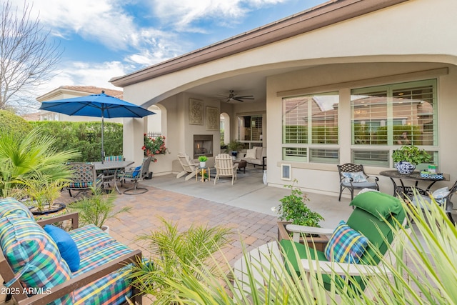 view of patio / terrace with a ceiling fan, a warm lit fireplace, and outdoor dining area