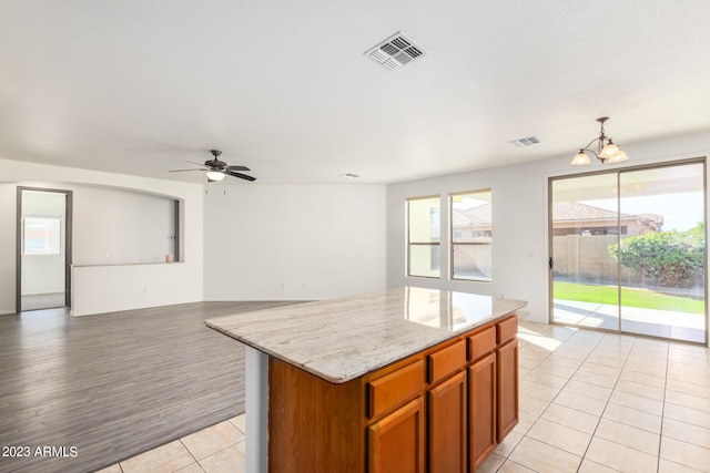 kitchen featuring ceiling fan with notable chandelier, a center island, light tile patterned floors, light stone countertops, and decorative light fixtures