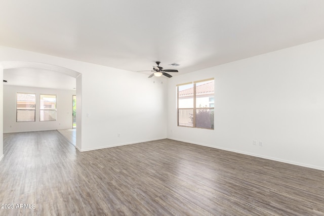 empty room with a wealth of natural light, dark hardwood / wood-style floors, and ceiling fan