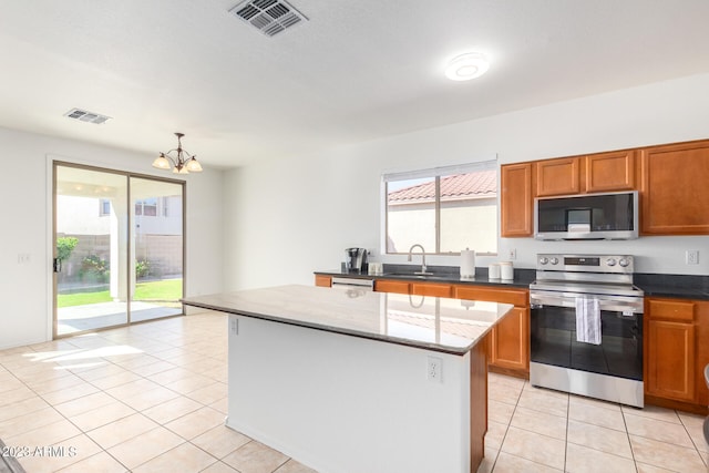 kitchen featuring dark stone counters, an inviting chandelier, light tile patterned flooring, a kitchen island, and appliances with stainless steel finishes