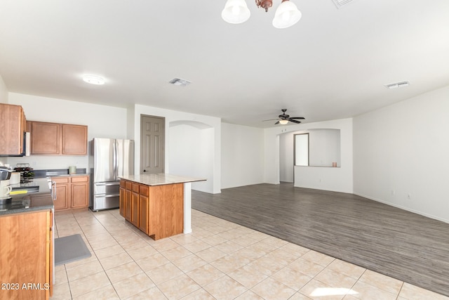 kitchen with stainless steel refrigerator, ceiling fan with notable chandelier, light hardwood / wood-style flooring, and a kitchen island