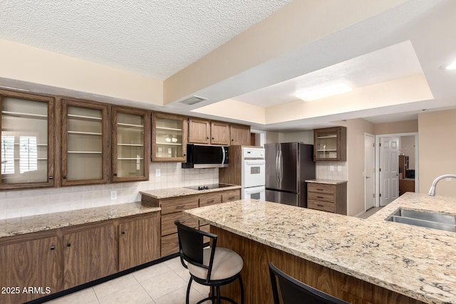 10126 W Sombrero Cir, Sun City, AZ 85373 - kitchen with freestanding refrigerator, a sink, a tray ceiling, backsplash, and black electric cooktop
