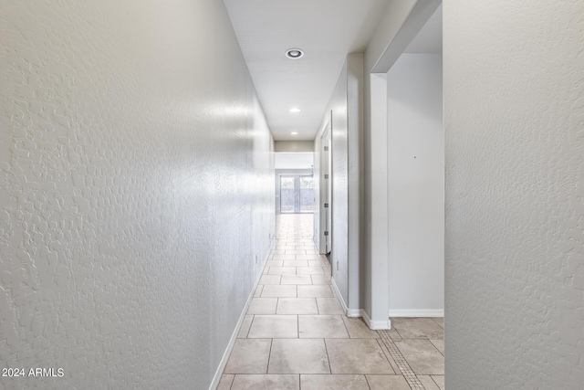 corridor featuring recessed lighting, a textured wall, baseboards, and light tile patterned floors