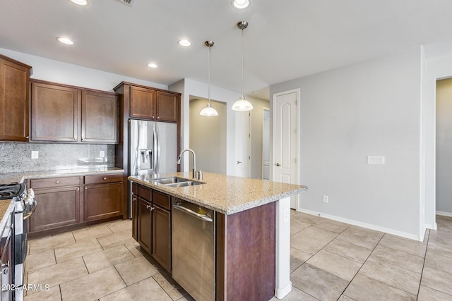 kitchen featuring light stone counters, stainless steel appliances, a sink, an island with sink, and pendant lighting