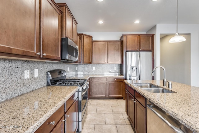 kitchen featuring light stone counters, a sink, hanging light fixtures, appliances with stainless steel finishes, and backsplash