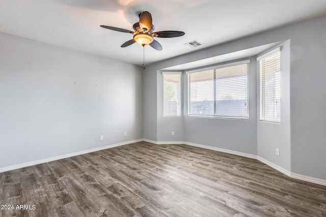 empty room with a ceiling fan, visible vents, baseboards, and wood finished floors