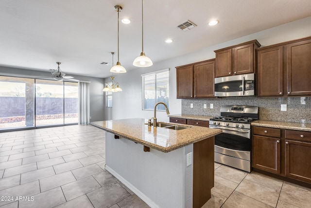 kitchen with a sink, visible vents, appliances with stainless steel finishes, light stone countertops, and pendant lighting