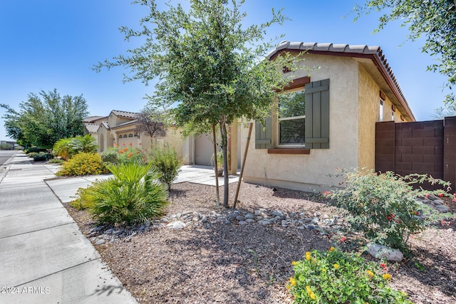 view of property exterior with an attached garage, fence, a tile roof, driveway, and stucco siding