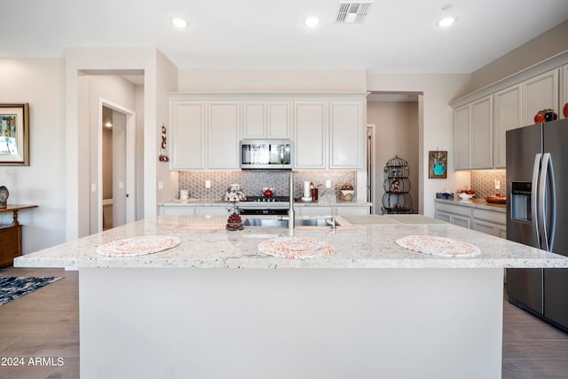 kitchen with appliances with stainless steel finishes, light stone countertops, and an island with sink