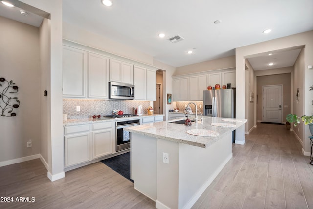 kitchen with light stone countertops, stainless steel appliances, white cabinetry, sink, and an island with sink