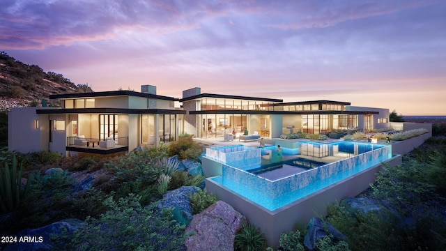 back house at dusk featuring a balcony and a patio area