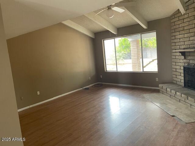 unfurnished living room featuring beamed ceiling, a brick fireplace, a ceiling fan, wood finished floors, and baseboards