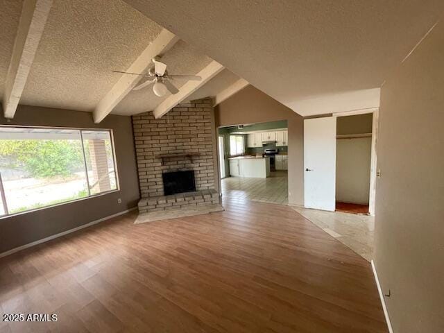 unfurnished living room featuring a textured ceiling, ceiling fan, light wood-style flooring, a fireplace, and baseboards