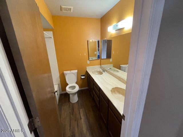 full bath featuring toilet, wood finished floors, baseboards, and double vanity
