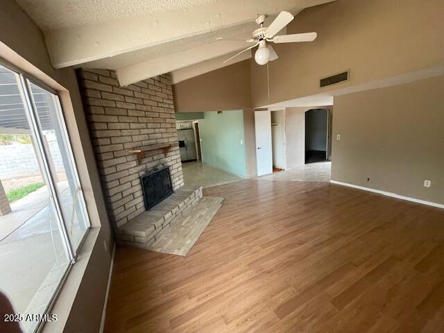 unfurnished living room with ceiling fan, light wood-type flooring, a fireplace, a textured ceiling, and high vaulted ceiling