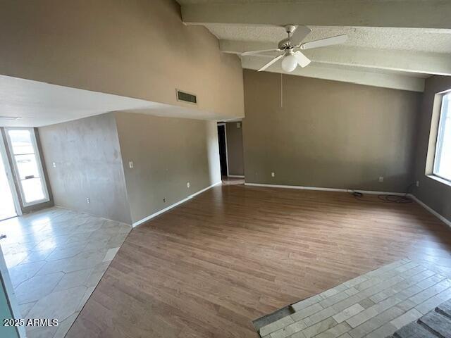 unfurnished room with plenty of natural light, a ceiling fan, beamed ceiling, wood finished floors, and baseboards