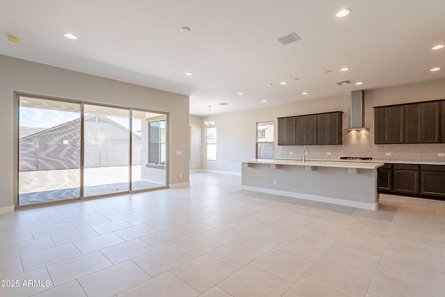 kitchen with light tile patterned floors, gas cooktop, a center island with sink, a kitchen bar, and wall chimney exhaust hood