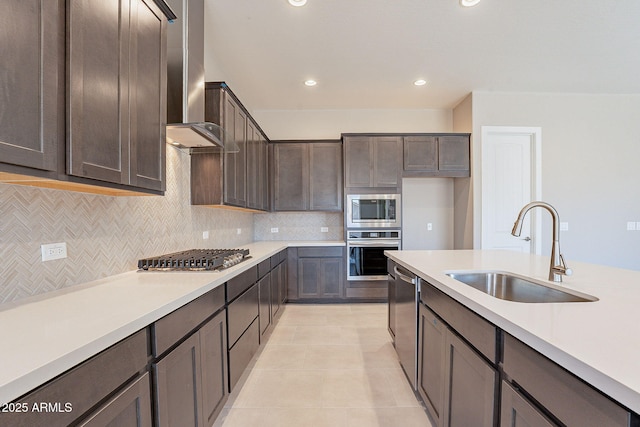 kitchen featuring sink, light tile patterned floors, dark brown cabinetry, stainless steel appliances, and wall chimney range hood